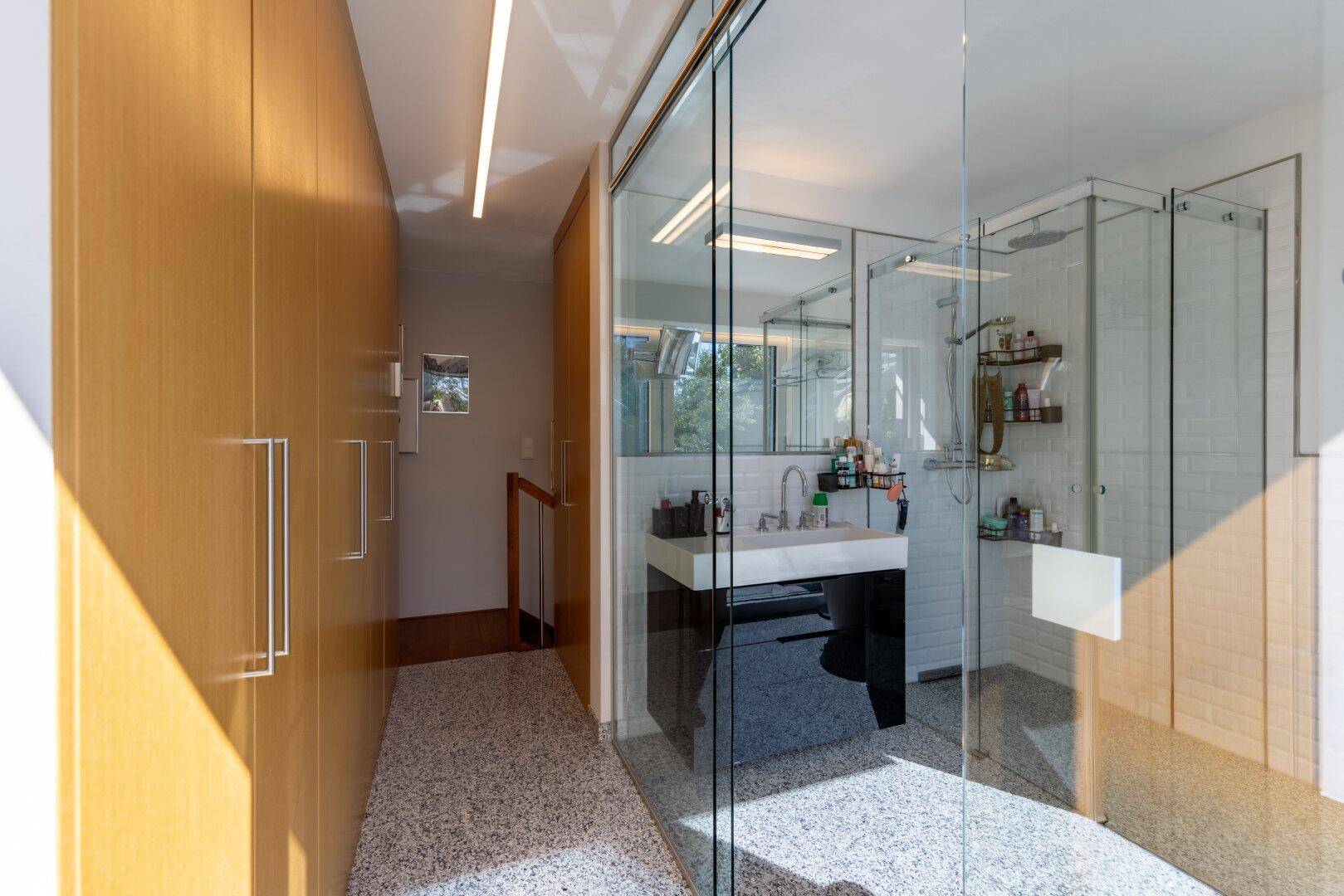 Heller Flur mit Einbauschränken führt zu einem modernen Badezimmer mit Glasdusche.