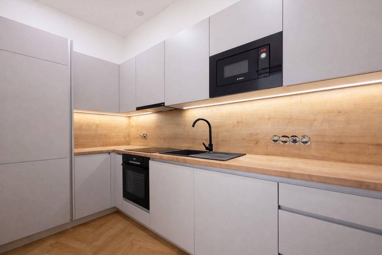 Moderne Einbauküche mit hellgrauen Schränken, Holz-Arbeitsplatte und integrierten Geräten.