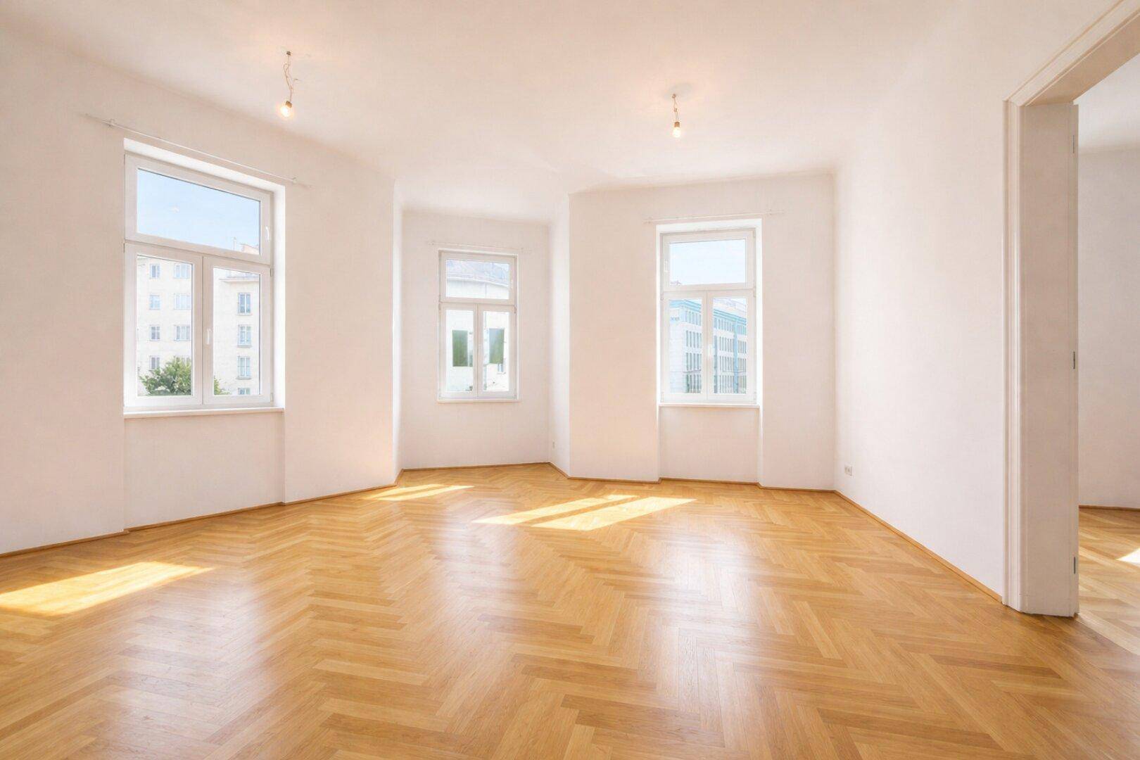 Geräumiges, helles Zimmer mit klassischem Fischgrätparkett und mehreren Fenstern, die viel Licht spenden.