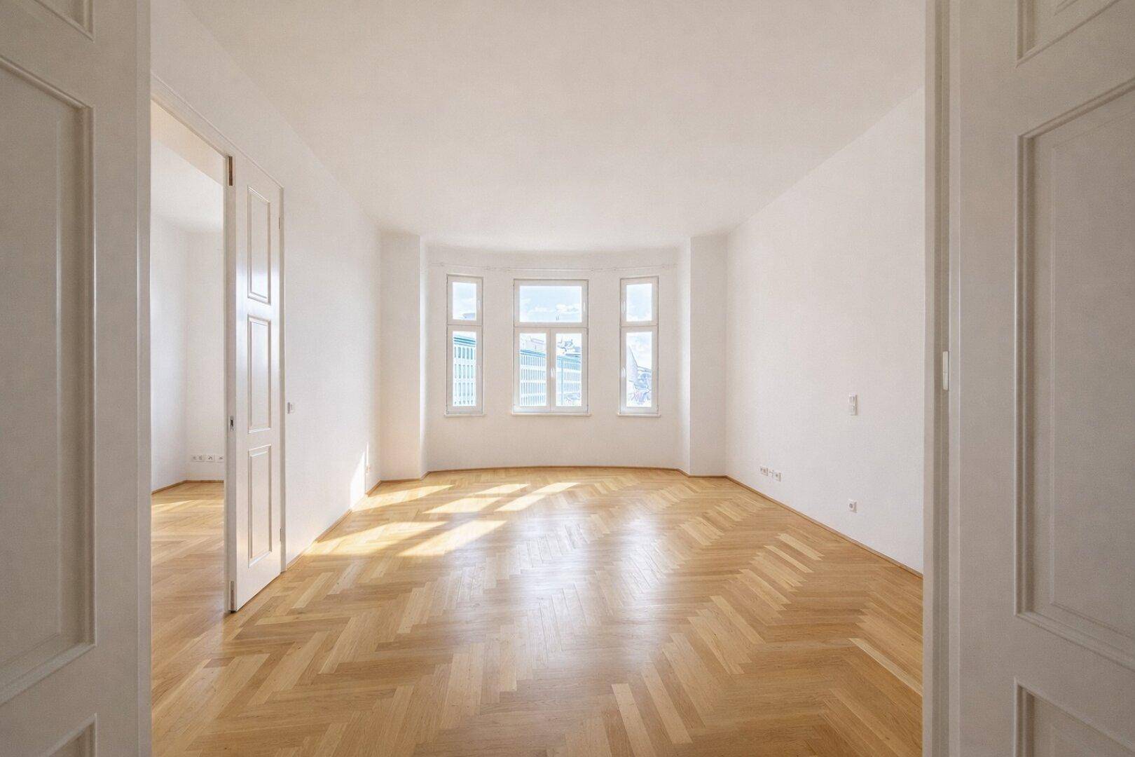 Helles, leeres Zimmer mit Fischgrätparkett, weißen Wänden und einem schönen Erkerfenster.