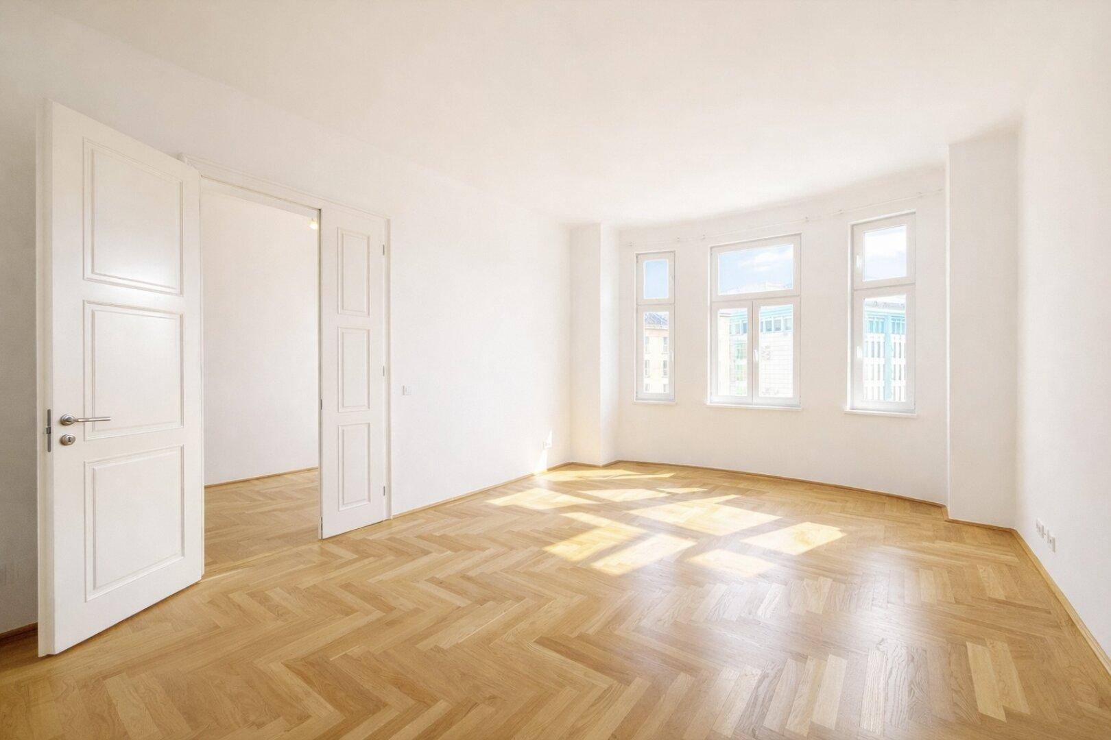Lichtdurchfluteter Raum mit elegantem Fischgrätparkett und großen Fenstern, bereit zur individuellen Gestaltung.