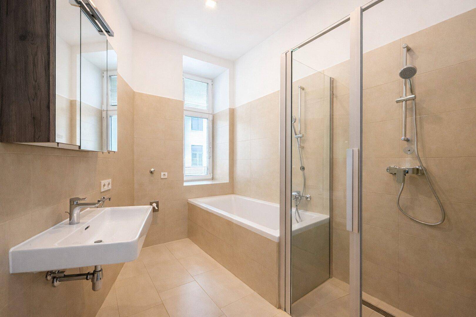 Modernes Badezimmer mit beigen Fliesen, Badewanne, begehbarer Dusche und Fenster für Tageslicht.