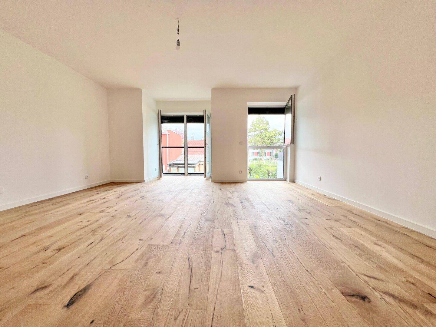 Geräumiges Wohnzimmer mit hellem Hartholzboden und großen Fenstern, die viel Tageslicht hereinlassen.