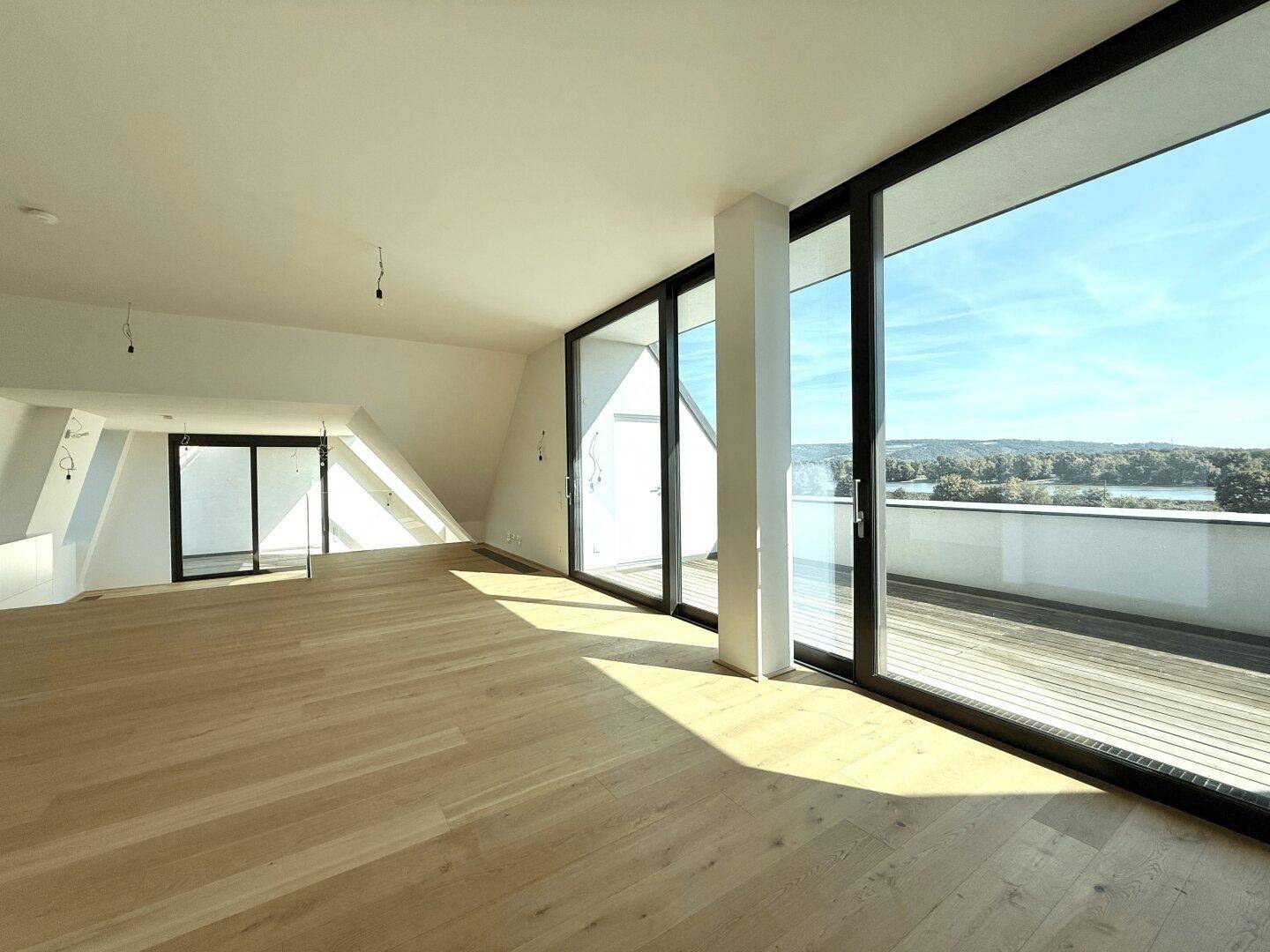Lichtdurchfluteter Wohnbereich mit Holzboden, großen Schiebefenstern und Panoramablick auf den See.
