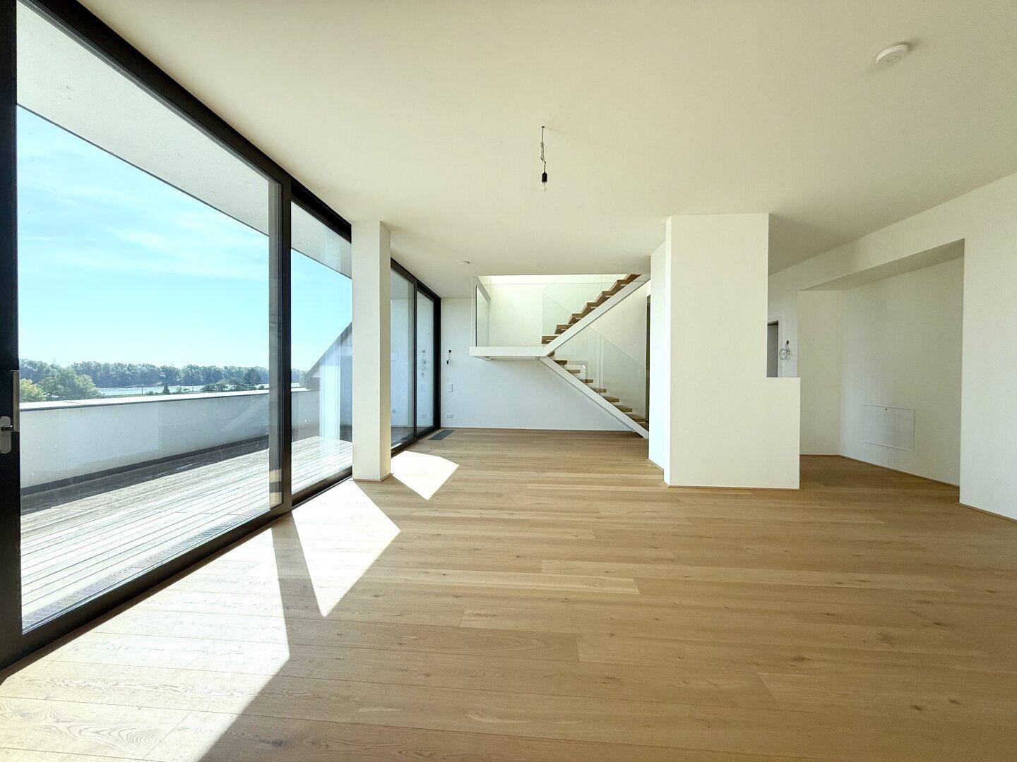 Helles, offenes Wohnzimmer mit großen Fensterfronten, Holzboden und weitem Blick auf die Umgebung.