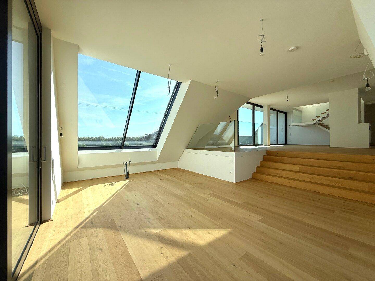 Geräumiger Wohnbereich mit Holzboden, moderner Treppe und großen Dachfenstern für viel Tageslicht.