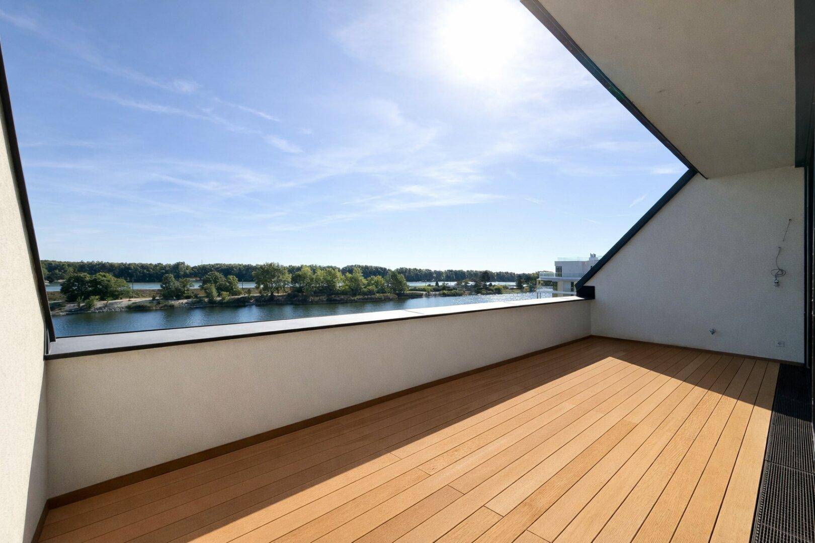 Heller Balkon mit Holzboden und weitem Blick auf den See unter strahlend blauem Himmel.
