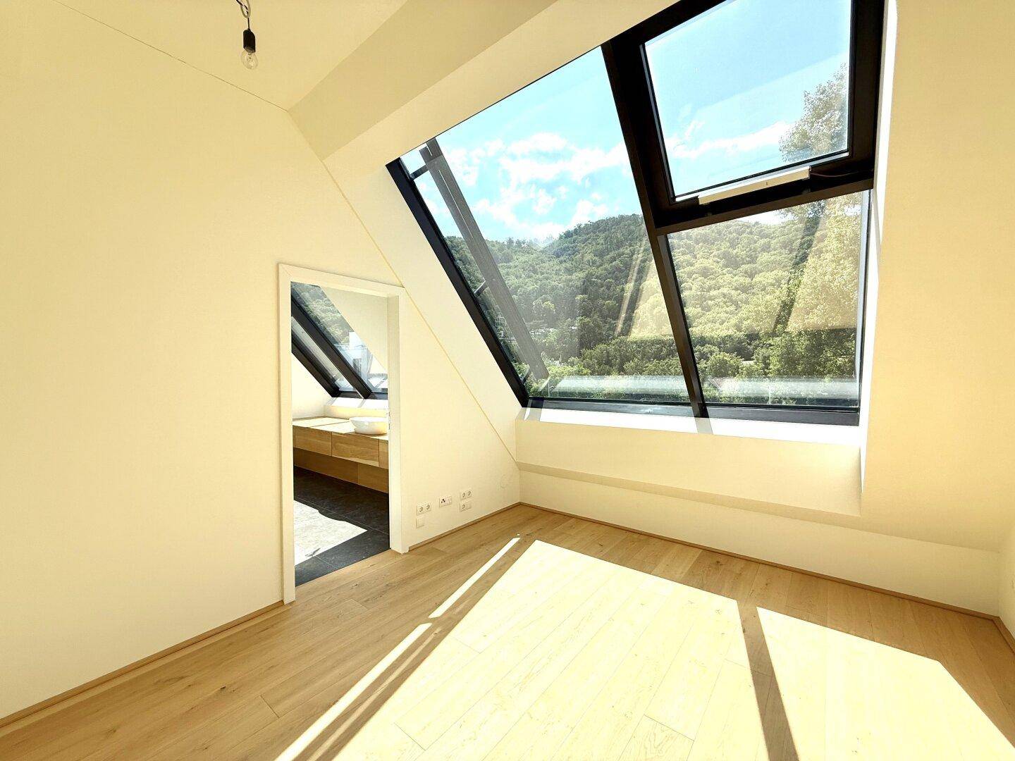 Helles Schlafzimmer mit Holzboden, großem Dachfenster und Zugang zu einem modernen Bad.