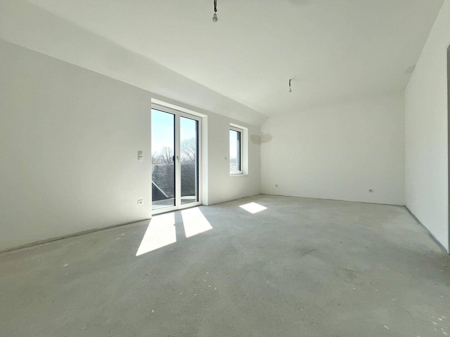 Heller, unmöblierter Raum mit großen Fenstern und viel Tageslicht, bereit für den Ausbau.