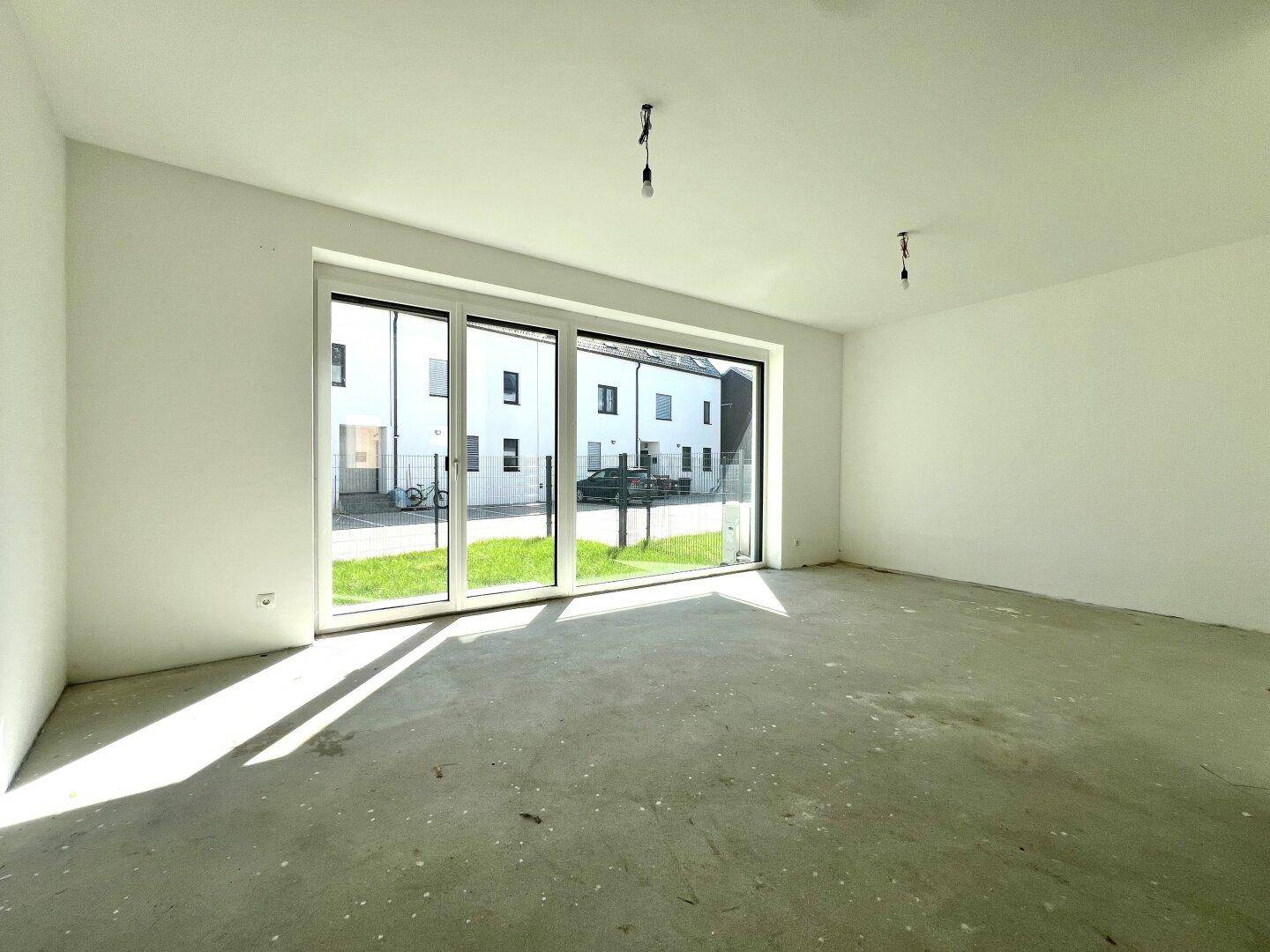 Heller, unmöblierter Wohnraum mit großen Fenstern und Blick auf die gegenüberliegenden Häuser.