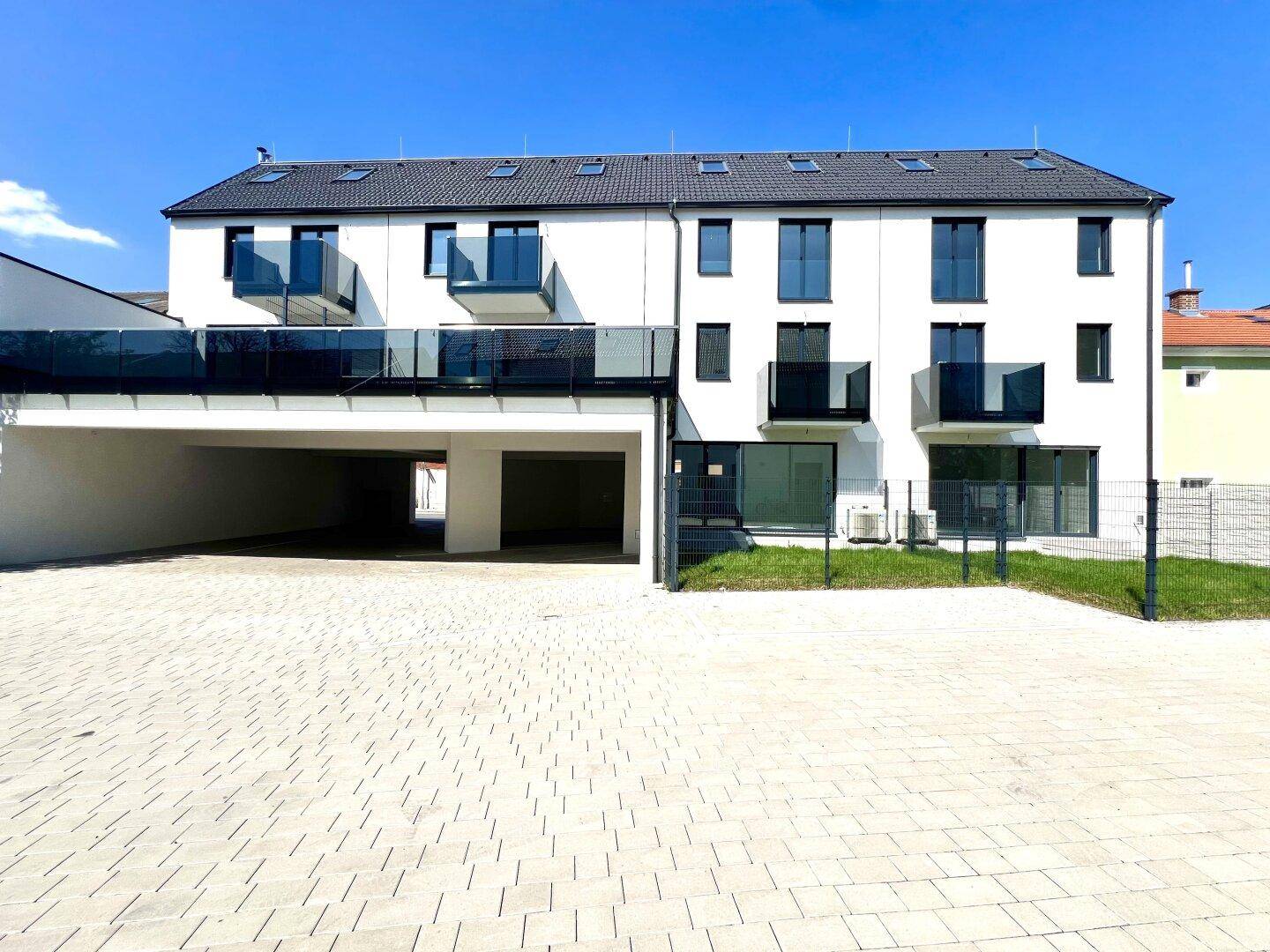 Moderne Wohnanlage mit weißer Fassade, Balkonen und überdachten Parkplätzen im Freien.