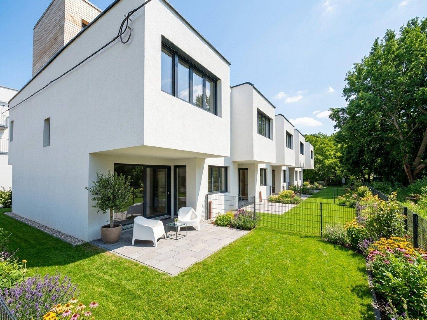 Moderne Reihenhäuser mit weißen Fassaden, privaten Gärten und einer gepflasterten Terrasse mit Sitzgelegenheiten.