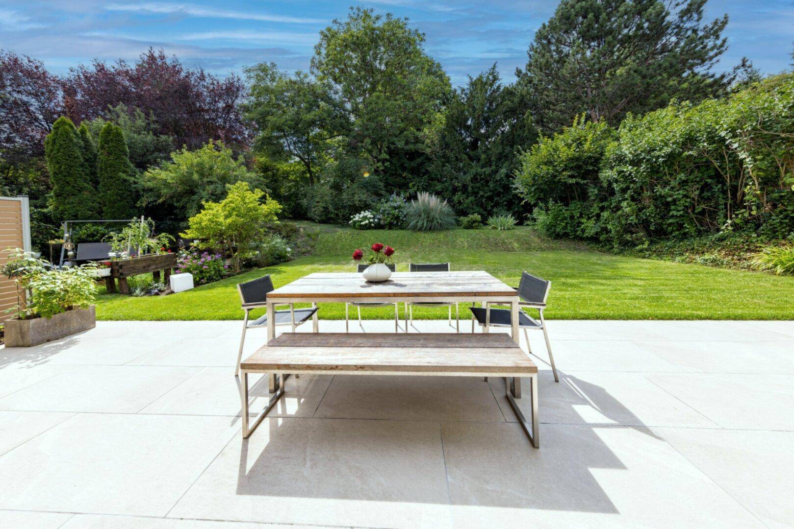 Geräumige Terrasse mit modernem Esstisch und Sitzbank, umgeben von einem grünen Garten.
