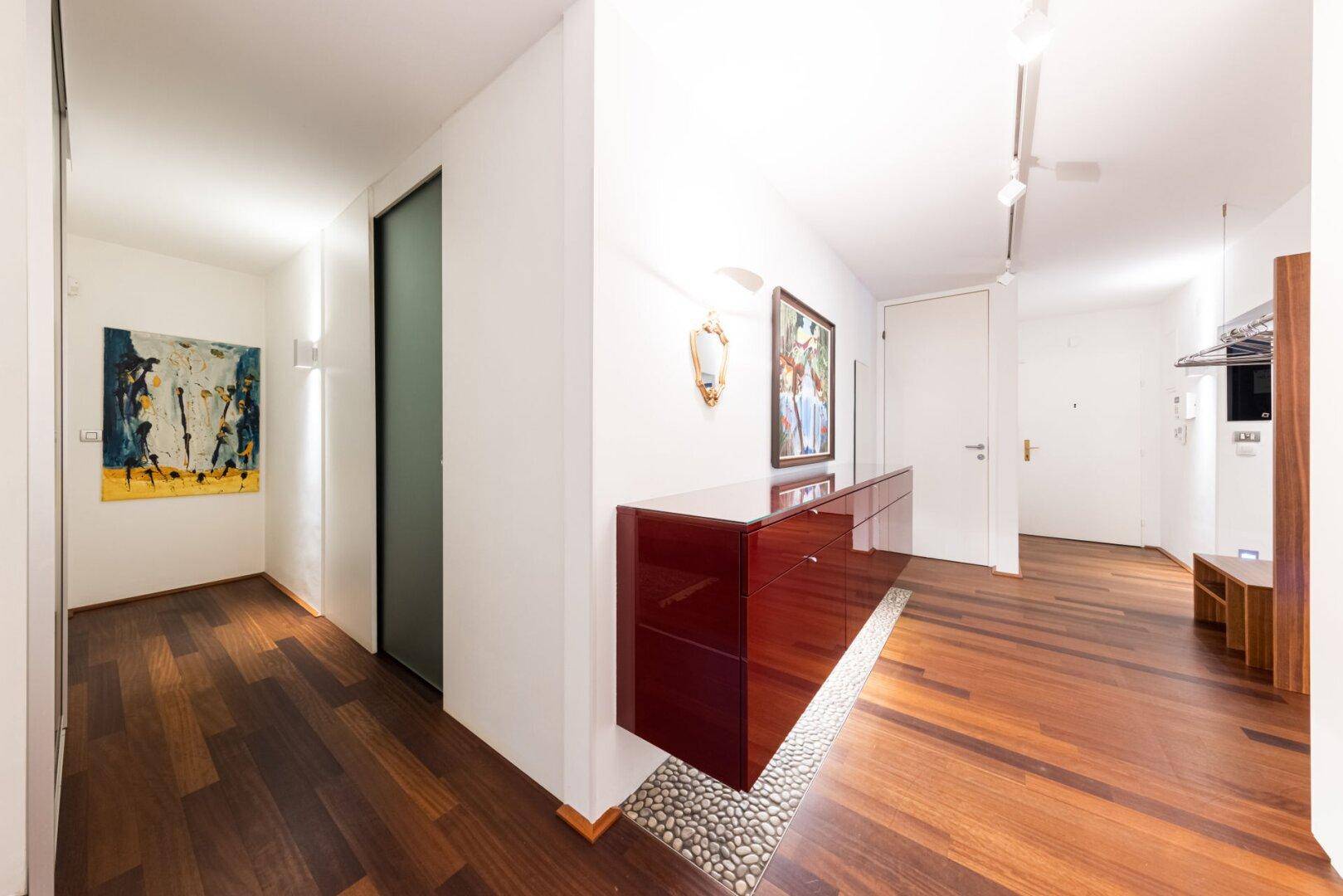 Moderner Flur mit schwebendem Sideboard und Holzboden, der zum Eingangsbereich führt.