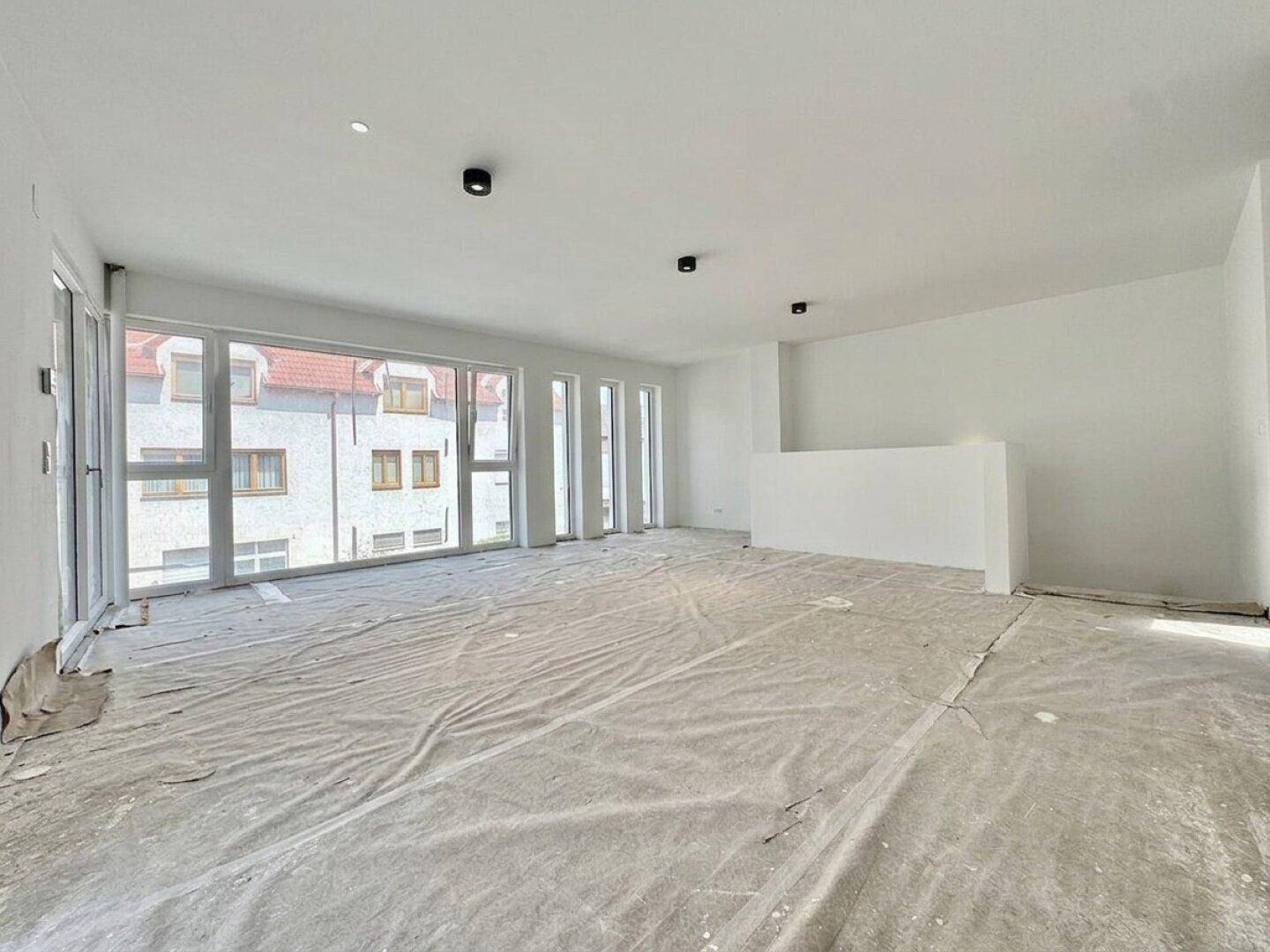 Großer, heller Wohnbereich in einem Neubau mit vielen Fenstern, bereit für individuelle Gestaltung.