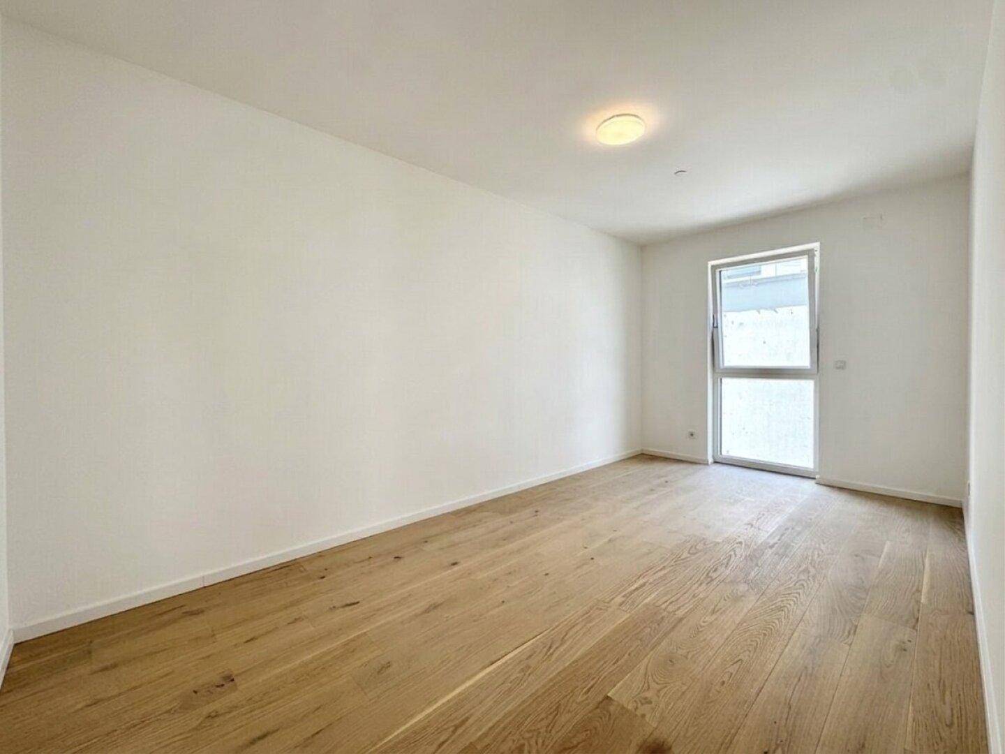 Helles Zimmer mit Echtholzboden und Fenster, ideal als Schlafzimmer oder Arbeitszimmer in einem Neubau.