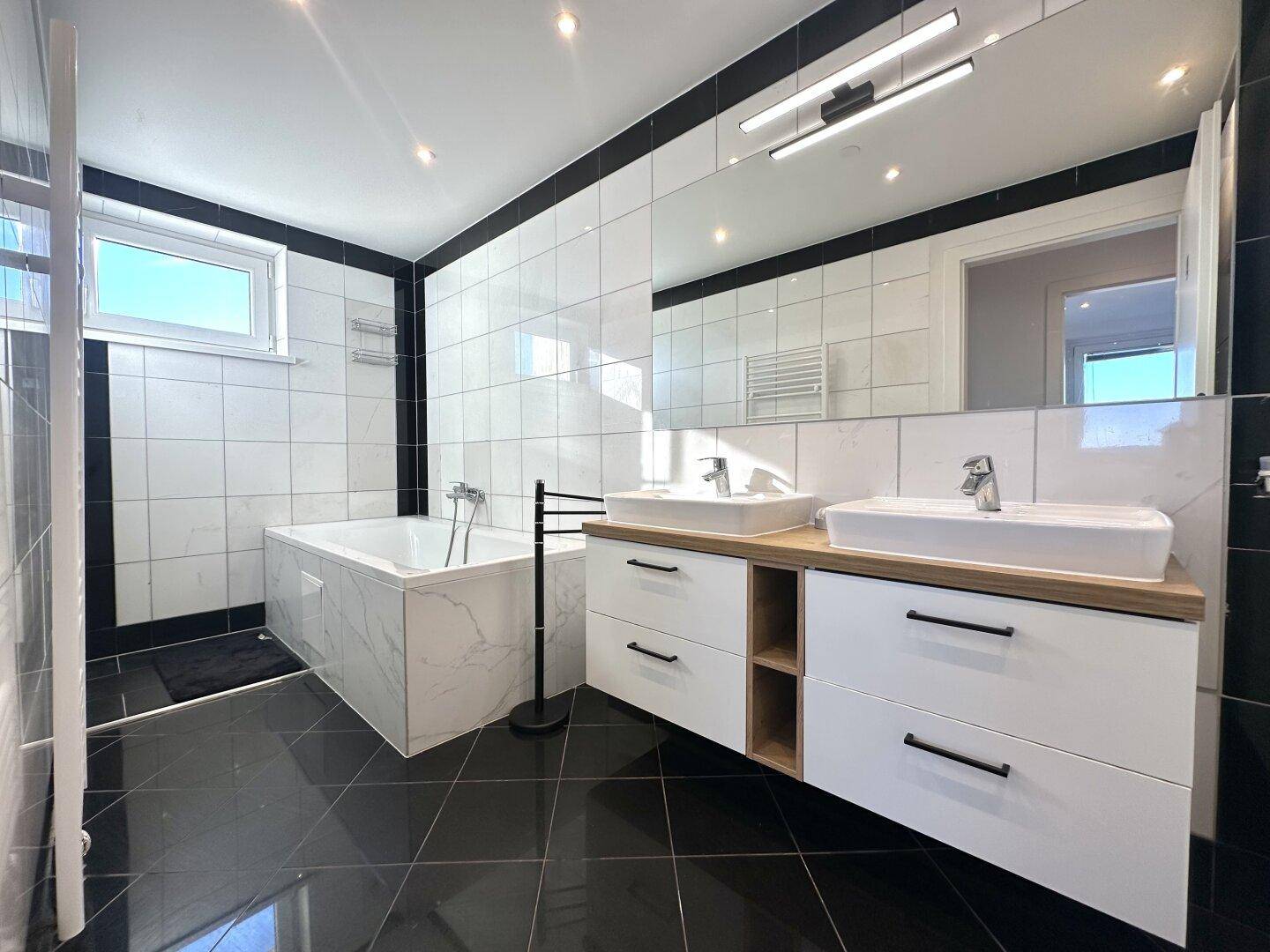 Modernes Badezimmer mit schwarzen Bodenfliesen, Doppelwaschbecken und Badewanne.