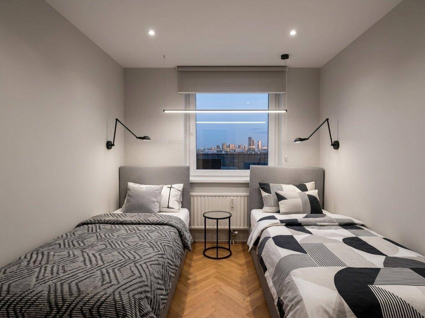 Gemütliches Schlafzimmer mit zwei Einzelbetten, Parkettboden und Stadtblick bei Nacht.