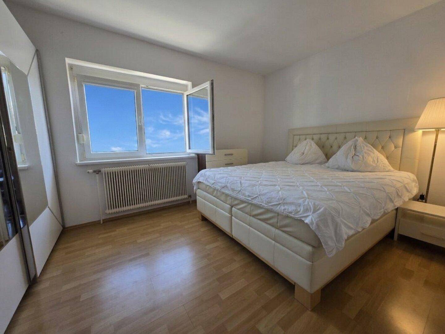 Helles Schlafzimmer mit Doppelbett, Holzfußboden und großem Fenster mit Blick nach draußen.