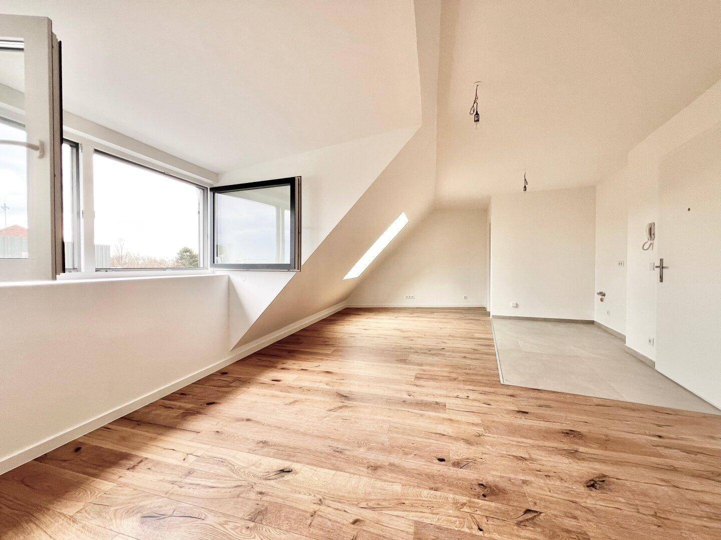Geräumiger Wohnbereich mit Holzboden, großer Fensterfront und schräger Dachschräge.