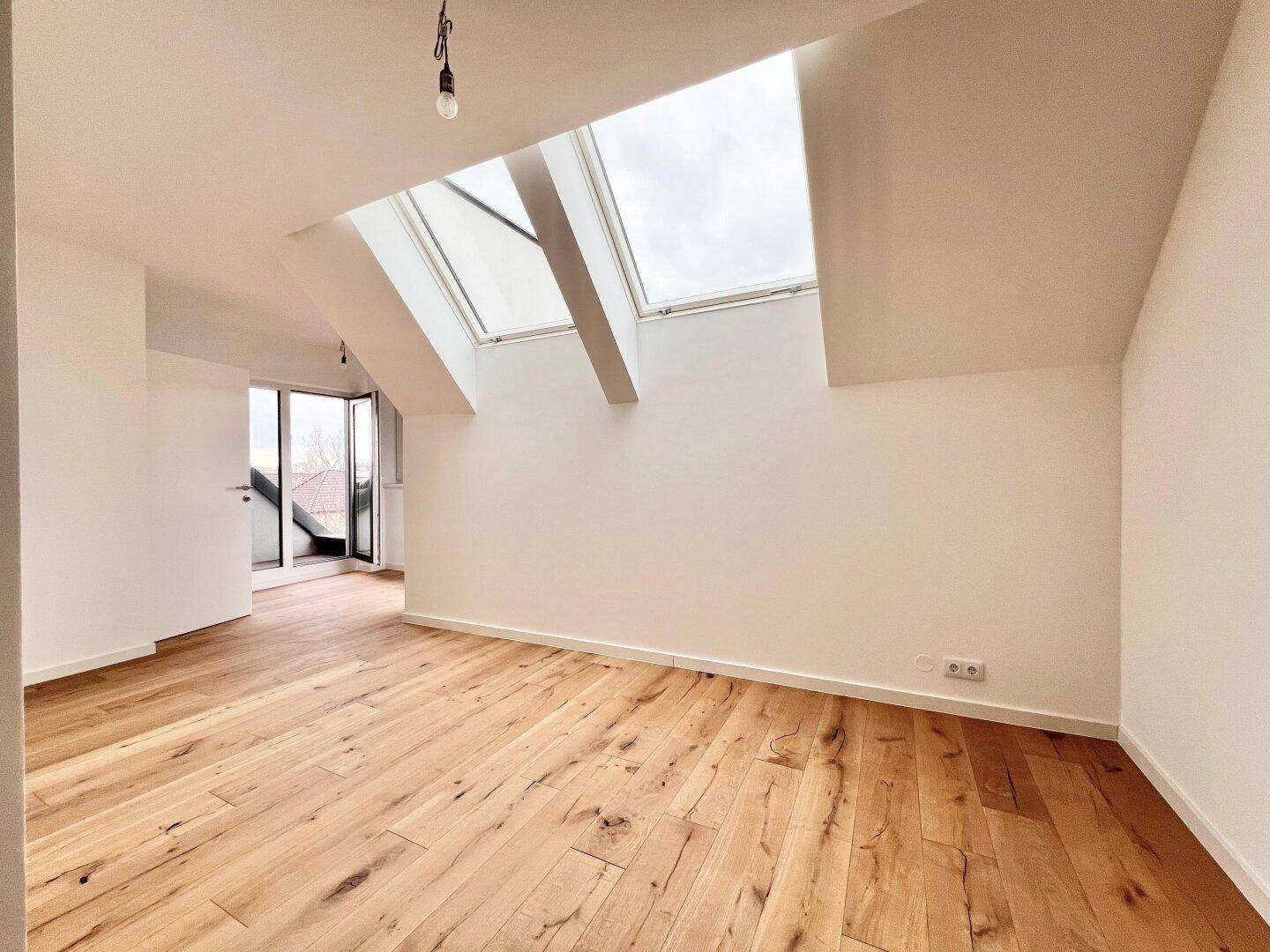 Heller Raum im Dachgeschoss mit Holzboden und zwei großen Dachfenstern.