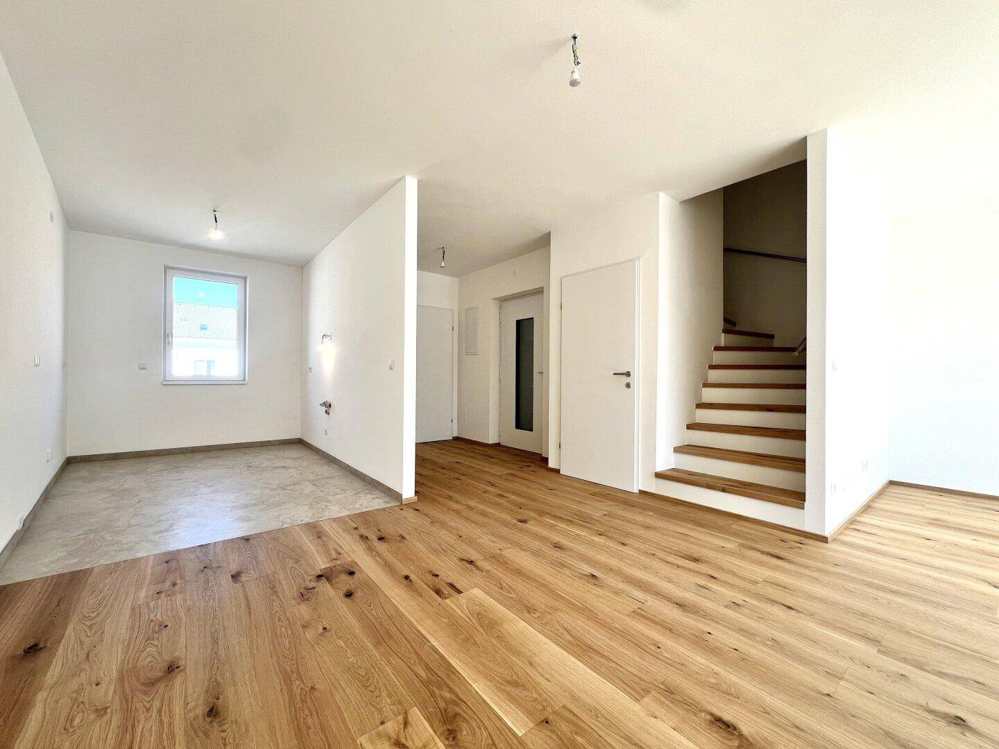 Eingangsbereich mit Holztreppe und Übergang zu einem weiteren Raum mit Fliesenboden.