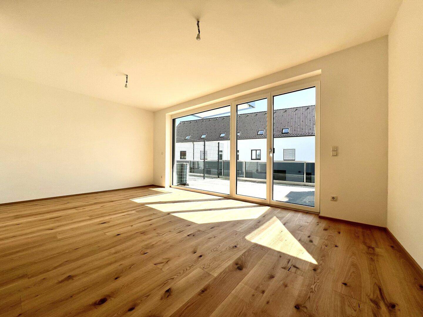 Lichtdurchfluteter Wohnraum mit hellem Parkettboden und breiter Fensterfront zur Terrasse.