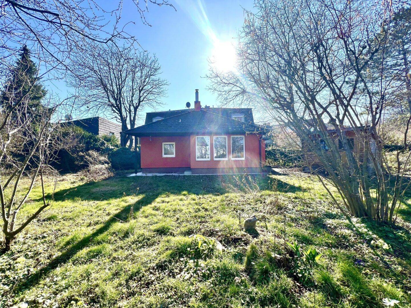 Sonniger Garten mit altem Baumbestand und Blick auf ein charmantes rotes Haus.