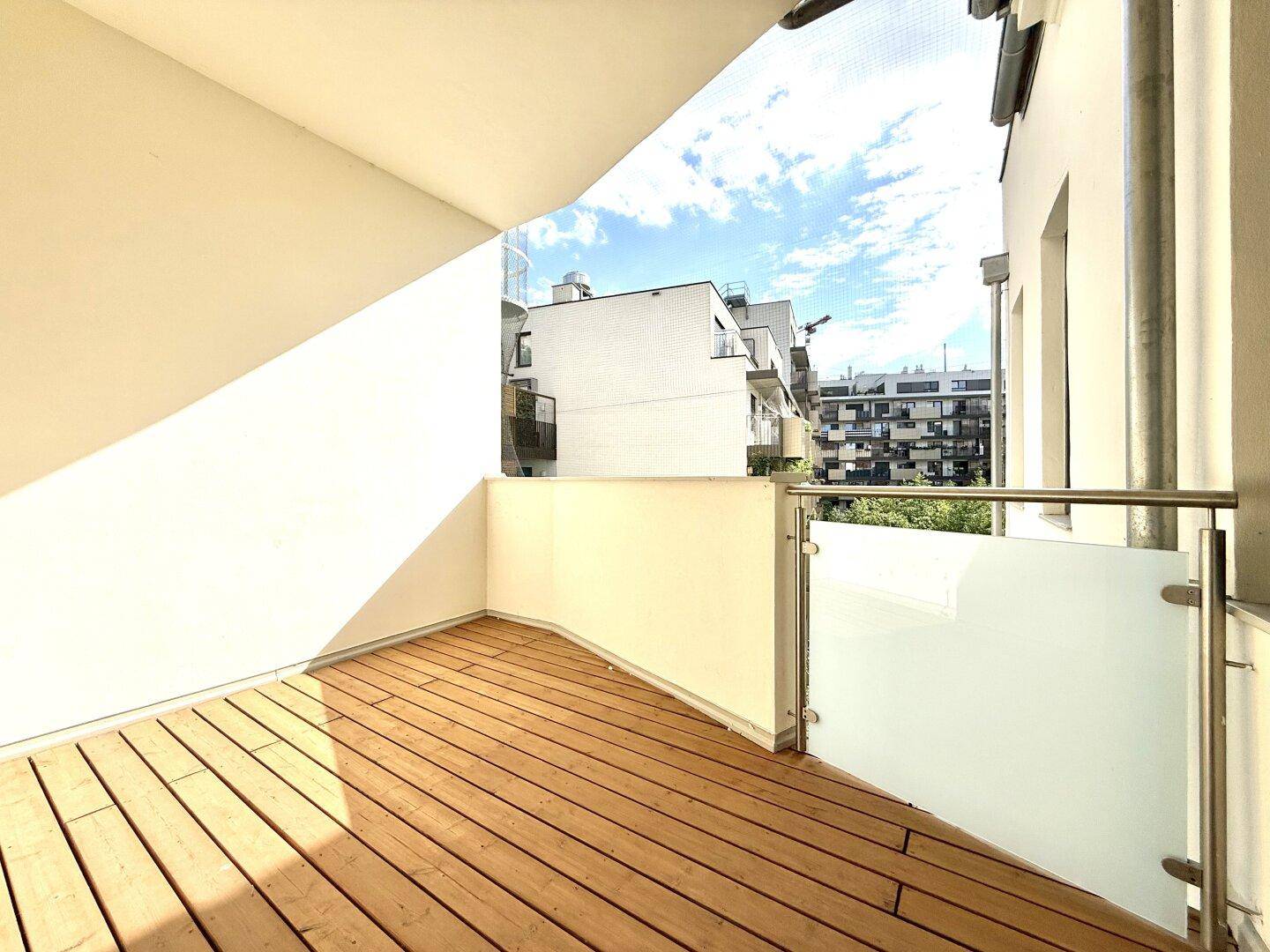 Geräumiger Balkon mit Holzboden und moderner Glasbrüstung, ideal für entspannte Stunden im Freien.