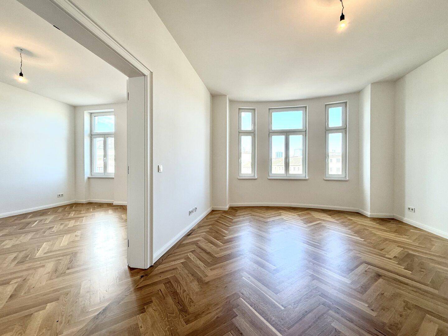 Helles, geräumiges Zimmer mit elegantem Fischgrätparkett und vielen Fenstern, die viel Tageslicht hereinlassen.