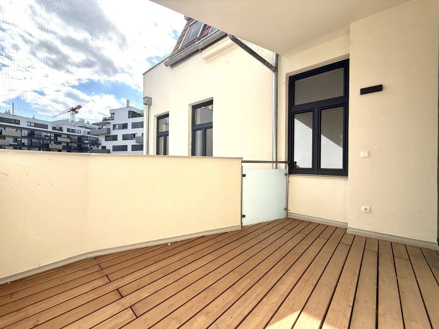 Moderner Balkon mit Holzfußboden und Glasgeländer, bietet einen Blick auf die umliegenden Gebäude.