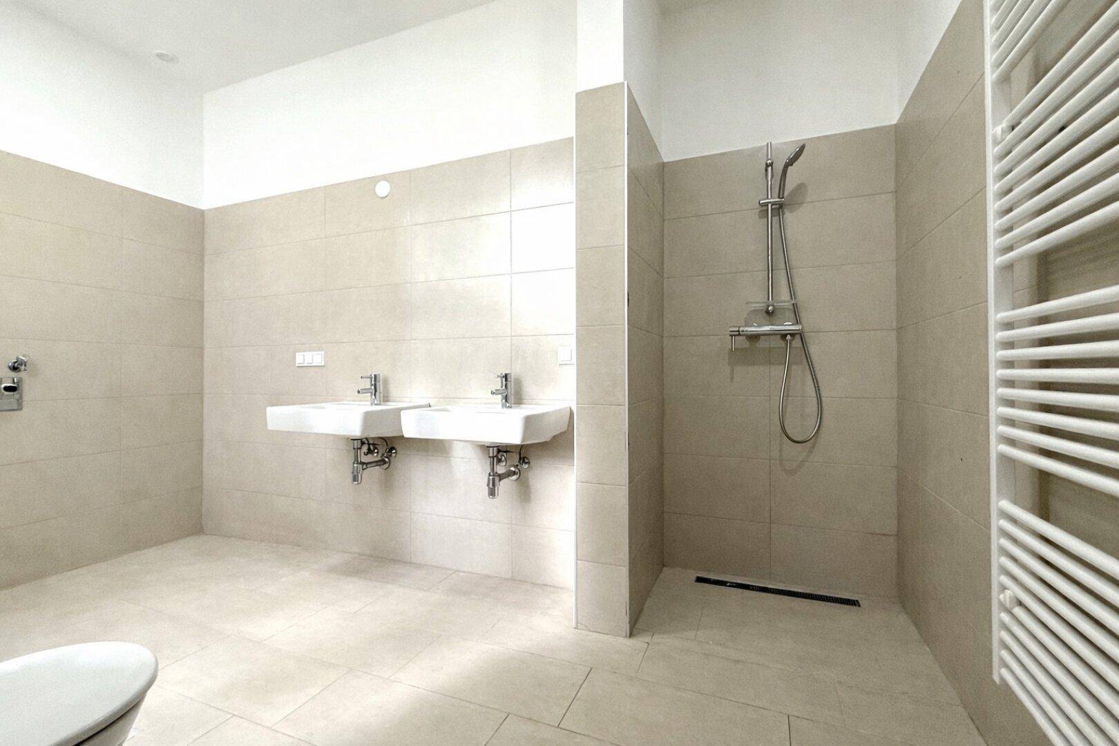 Modernes Badezimmer mit beigefarbenen Fliesen, zwei Waschbecken und einer ebenerdigen Dusche.