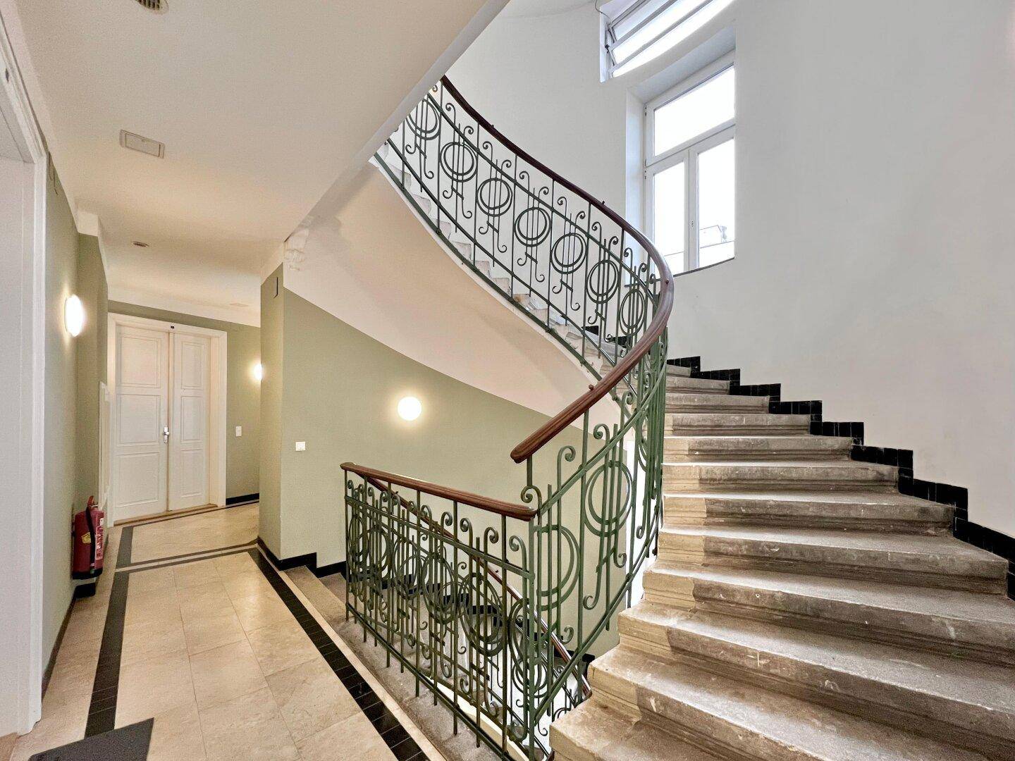 Historisches Treppenhaus mit eleganten Steinstufen und kunstvollem schmiedeeisernem Geländer in einem Altbau.