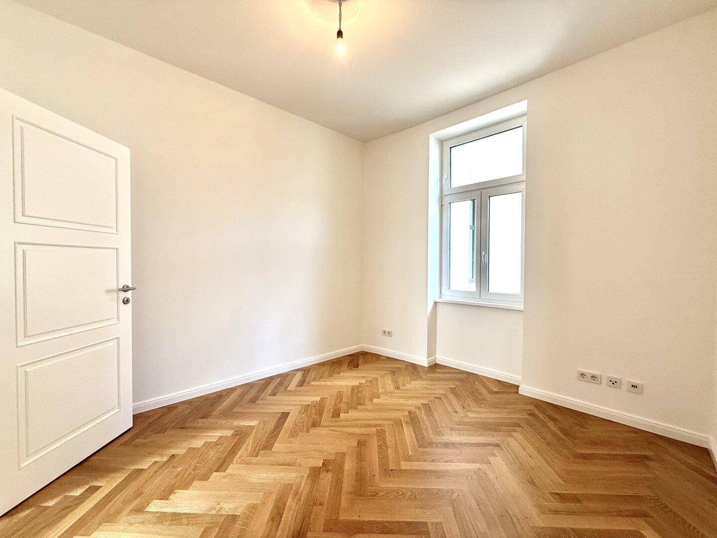 Gemütliches Zimmer mit Fischgrätparkett und einem großen Fenster, ideal als Schlaf- oder Arbeitszimmer.