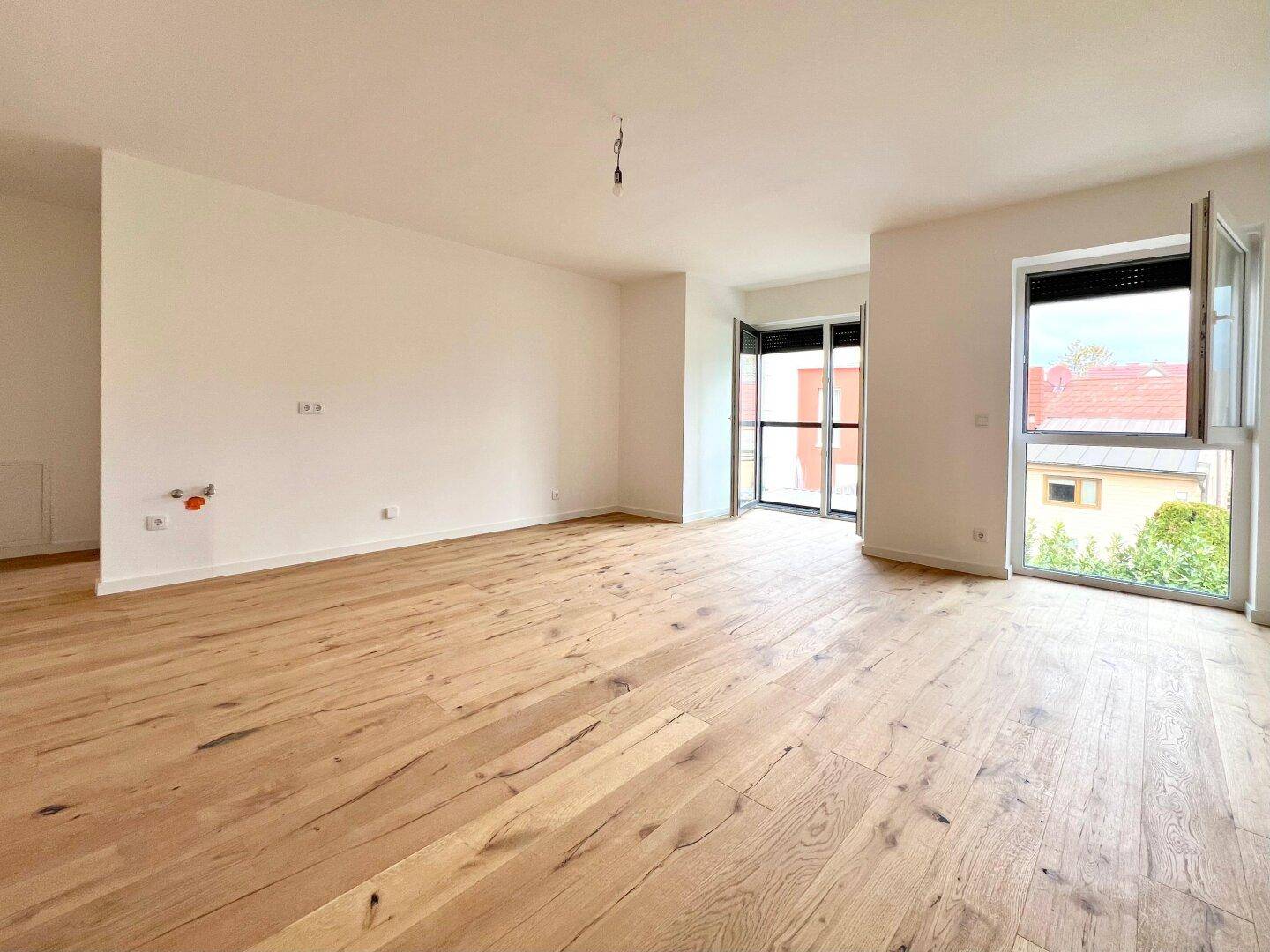 Geräumiger Wohnbereich mit hellem Holzboden und großen Fenstern für viel Tageslicht.