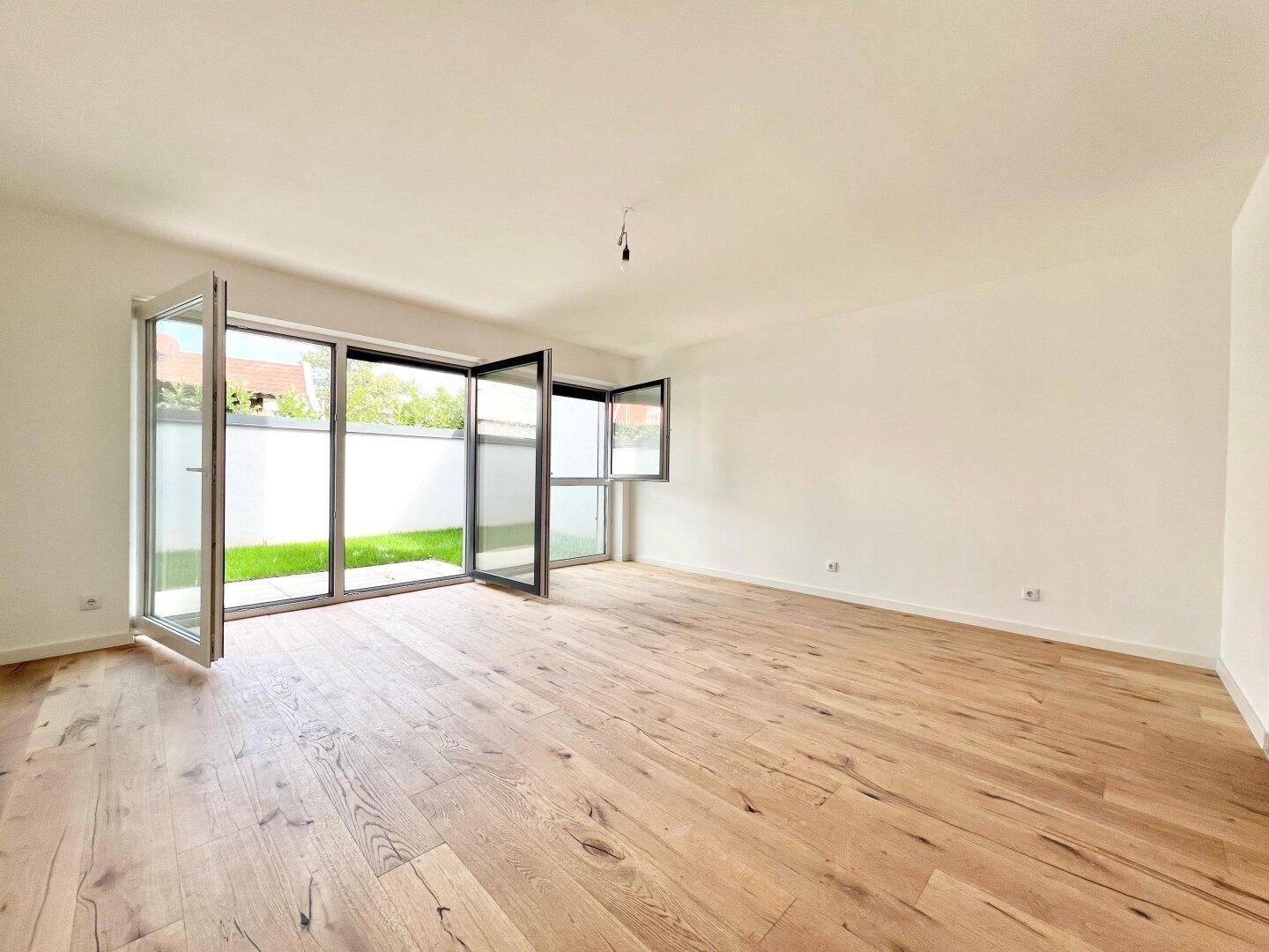 Heller Wohnraum mit Holzboden und großen Glastüren, die zum Garten führen.