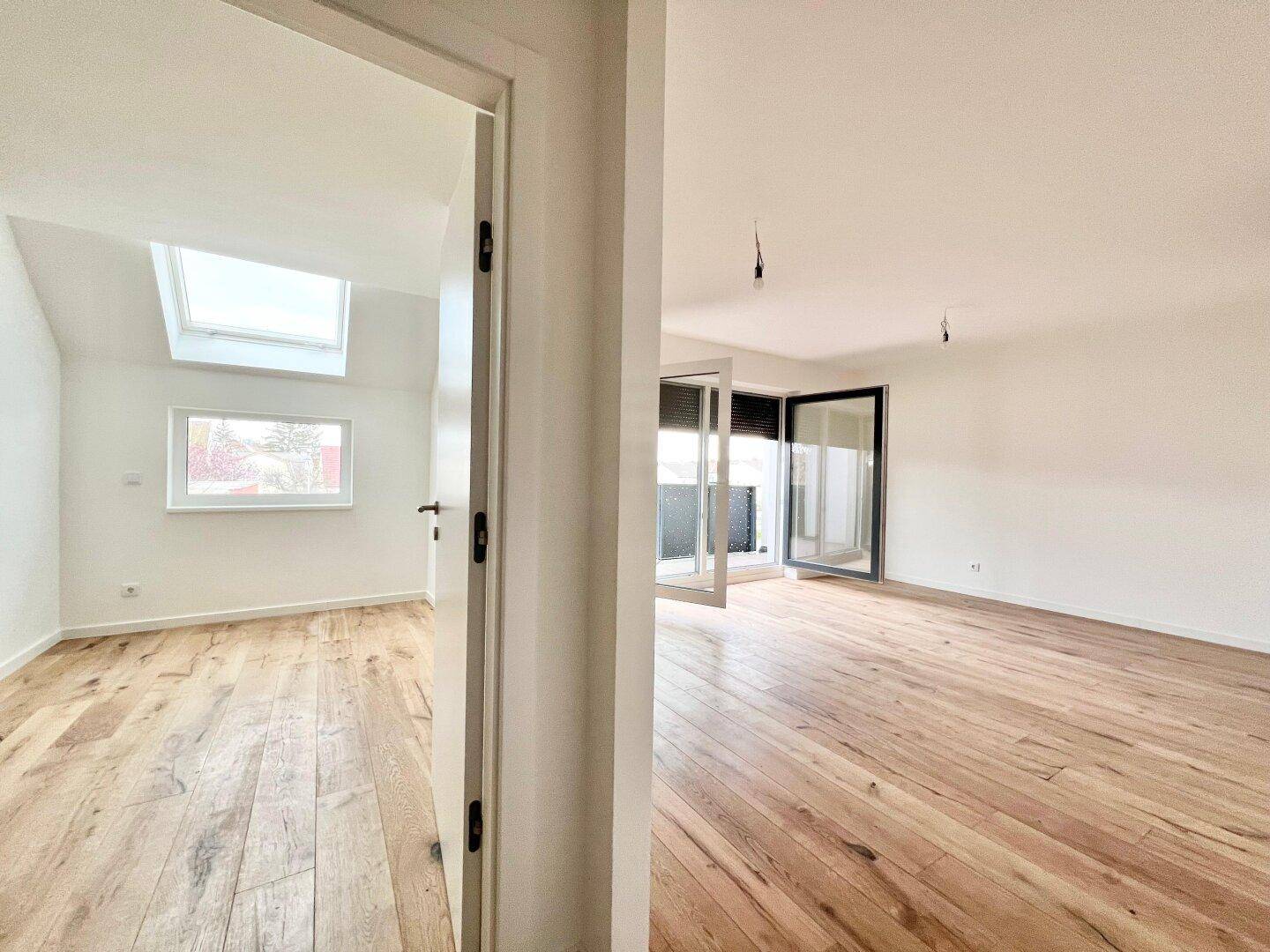 Blick in zwei helle Räume mit Holzboden, einer davon mit Dachfenster.