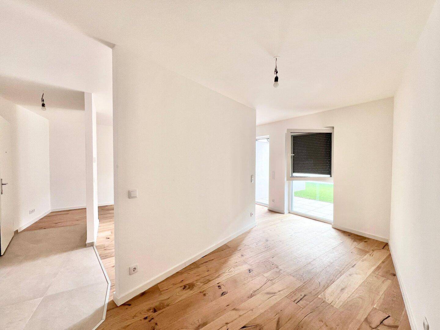 Lichtdurchfluteter Wohnbereich mit neuem Holzfußboden, weißen Wänden und Blick ins Grüne.