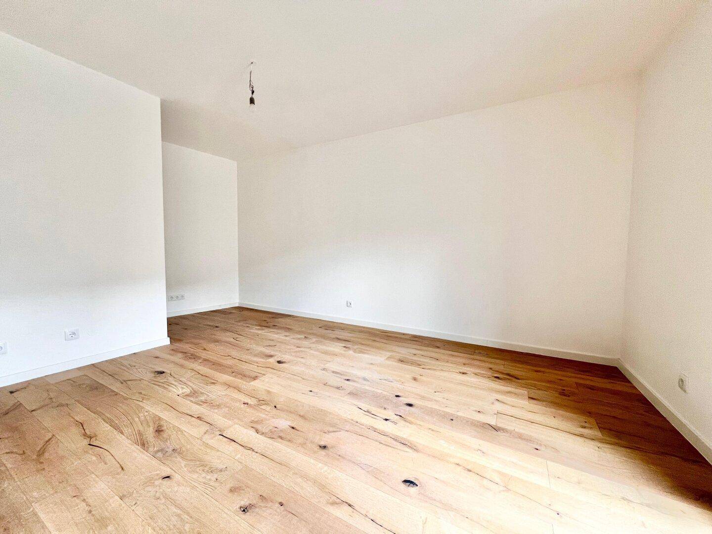 Geräumiger, leerer Wohnraum mit hellem Holzparkett und frisch gestrichenen Wänden, bereit zum Einzug.