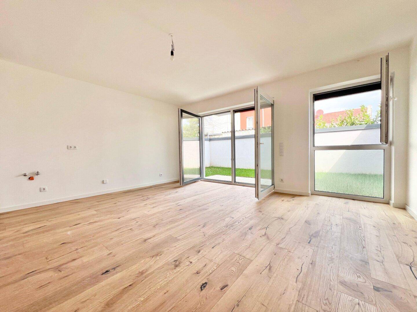 Geräumiger, heller Raum mit Holzboden und Zugang zu einem Außenbereich, ideal für Wohnküche.