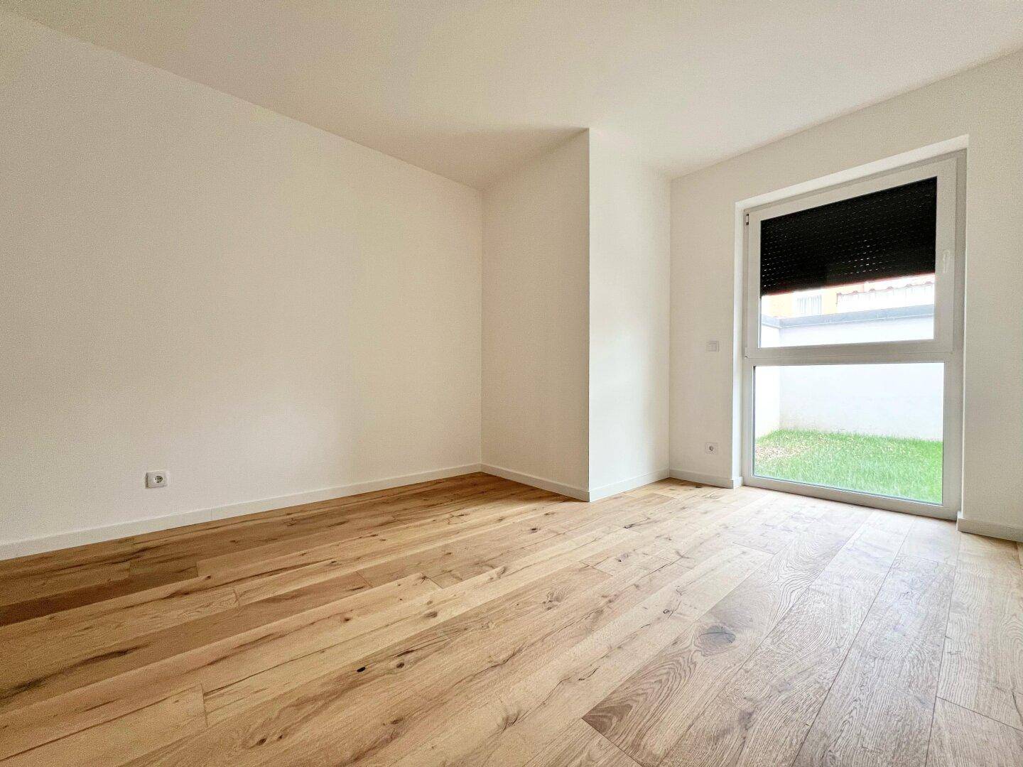 Helles Zimmer mit Holzboden und großem Fenster, das den Blick ins Grüne freigibt.