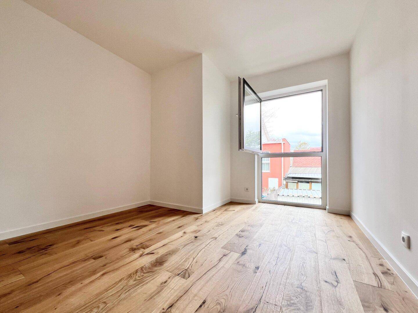 Helles Schlafzimmer mit Holzboden und einem Fenster, das viel Tageslicht hereinlässt.