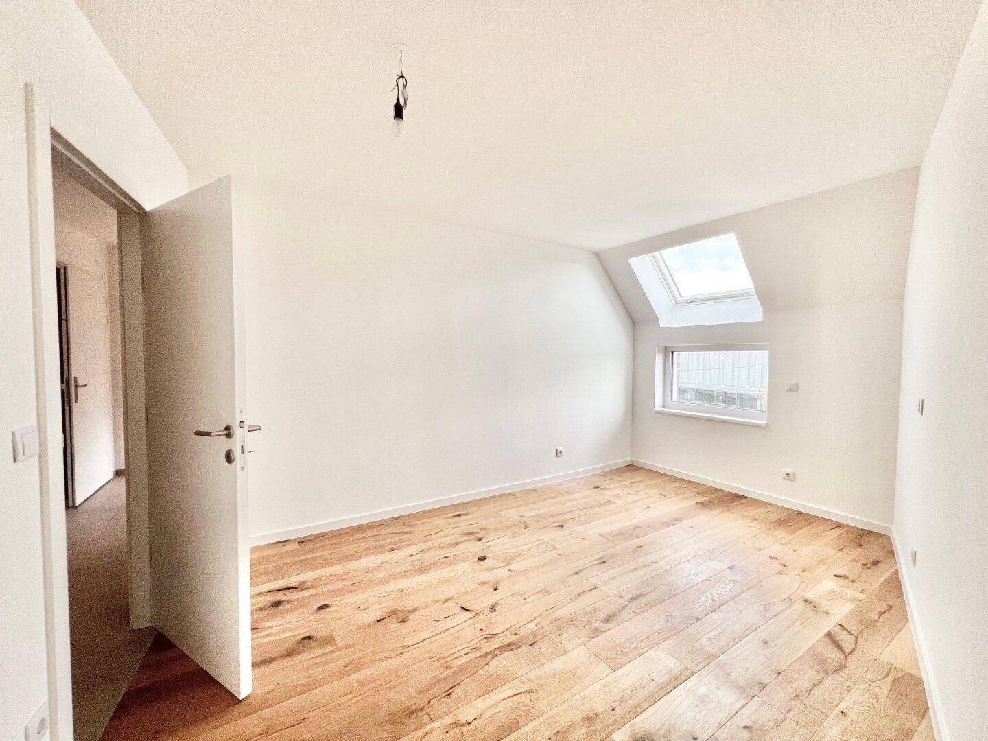 Helles Schlafzimmer im Dachgeschoss mit Holzboden, Dachfenster und schrägen Wänden.