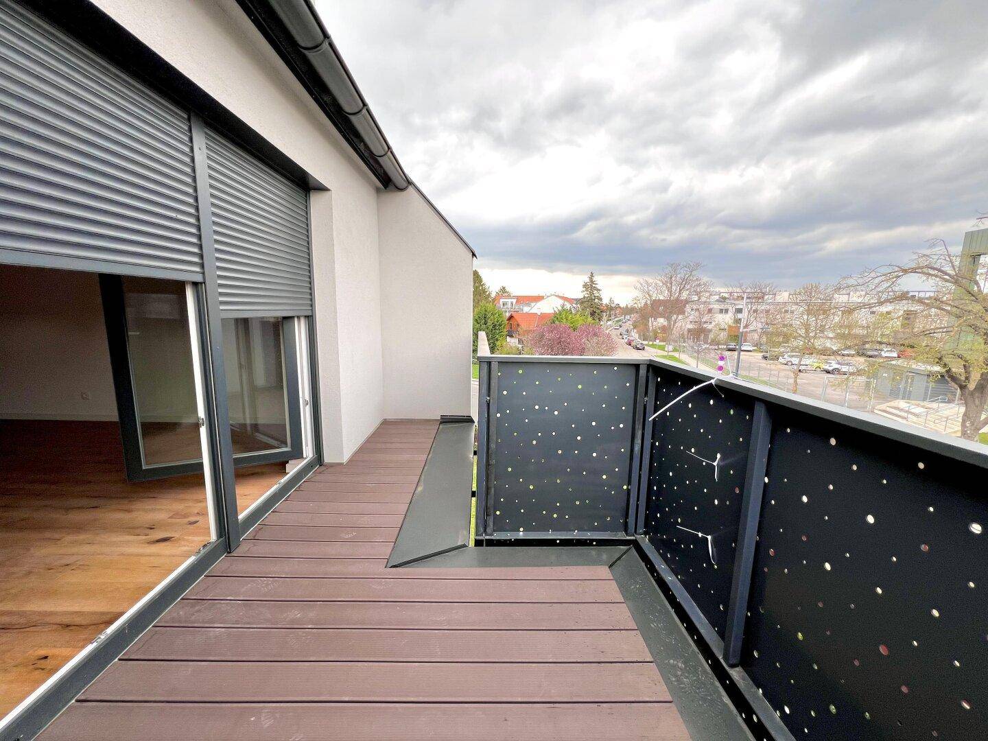 Moderner Balkon mit Holzdielen und Blick auf die Umgebung, ausgestattet mit Rollläden.