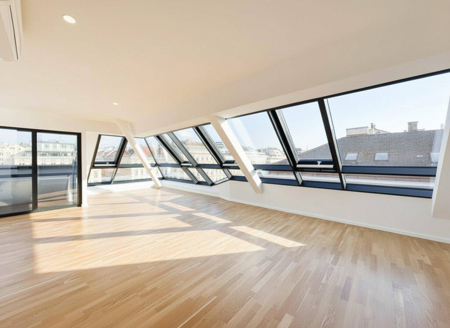 Geräumiges, unmöbliertes Wohnzimmer mit schrägen Dachfenstern und Holzboden.