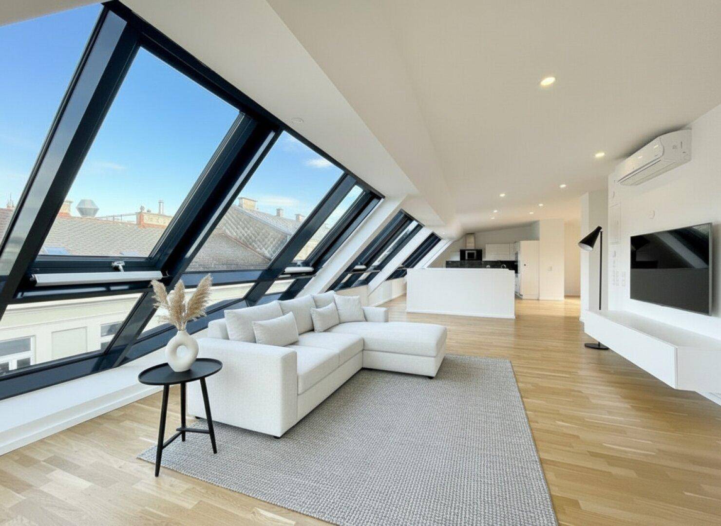 Modernes Wohnzimmer mit schrägen Fenstern, Holzboden und Blick auf die Stadt.