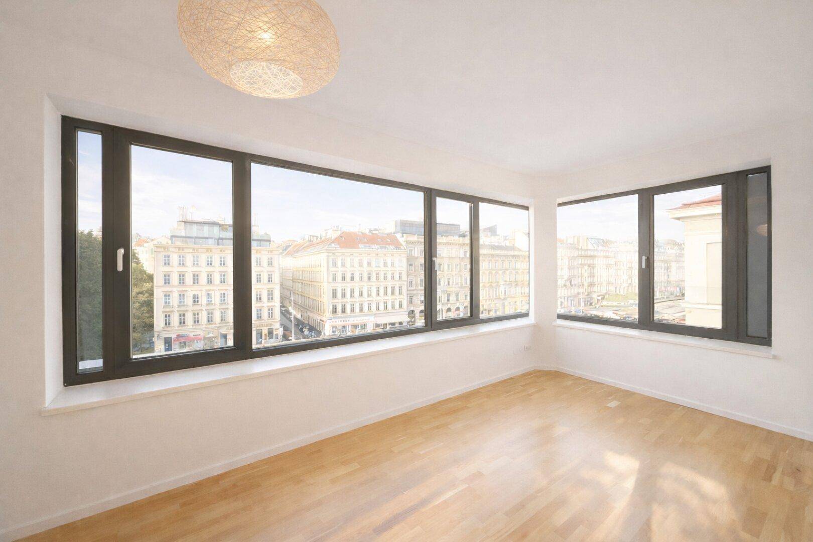Helles Zimmer mit Holzboden und großen Fenstern mit Stadtblick.