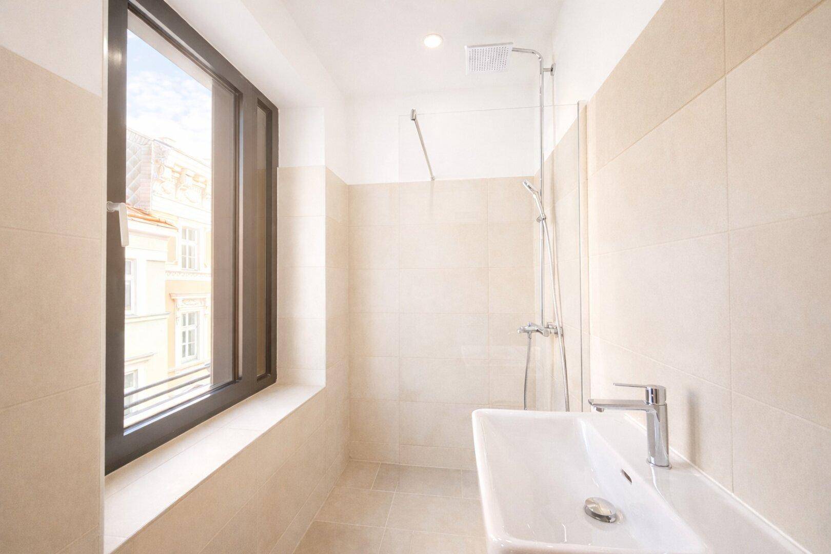 Helles Badezimmer mit beigen Fliesen, Dusche und Einzelwaschbecken.