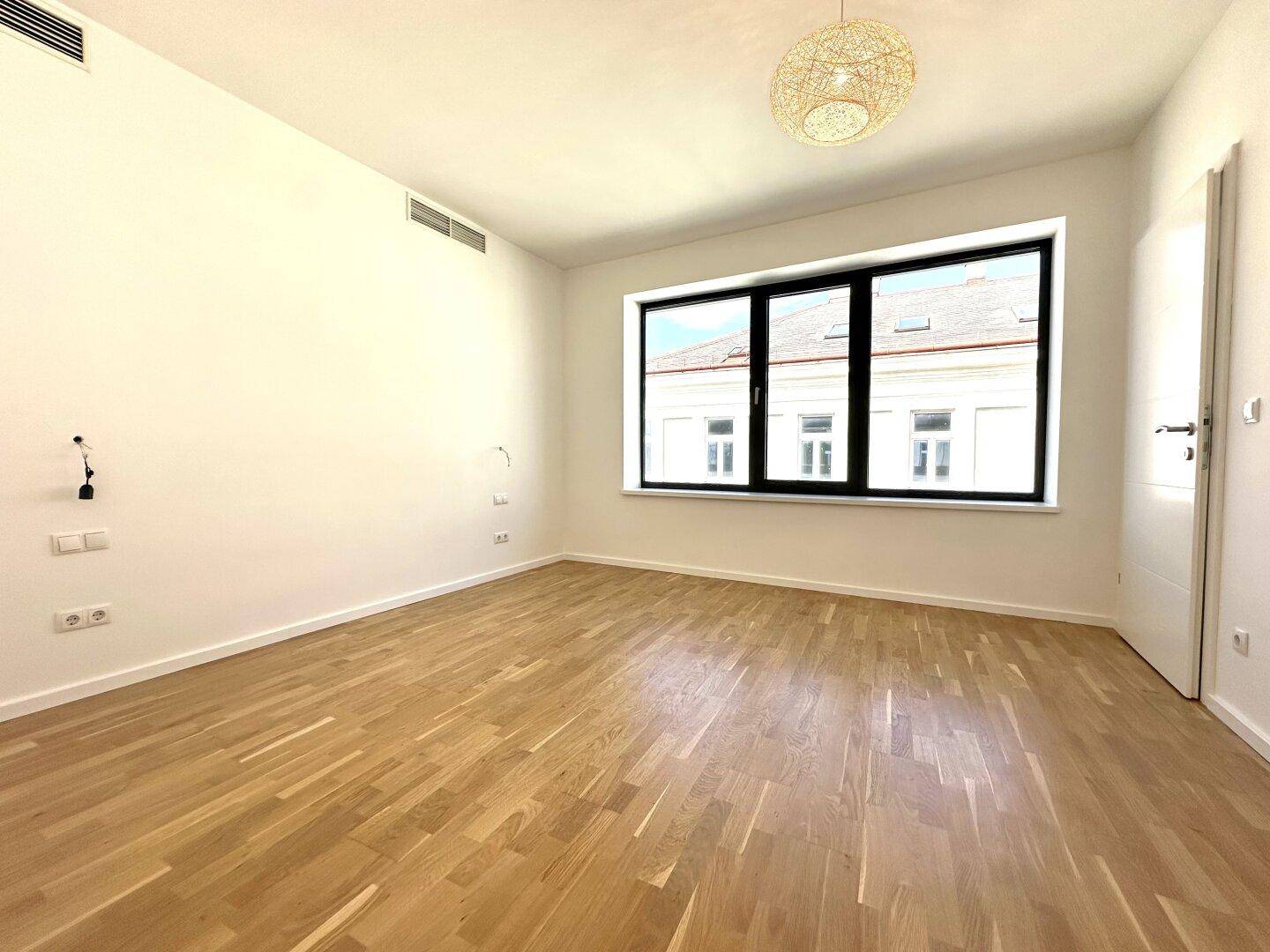 Geräumiges, unmöbliertes Schlafzimmer mit Holzboden und großen Fenstern.