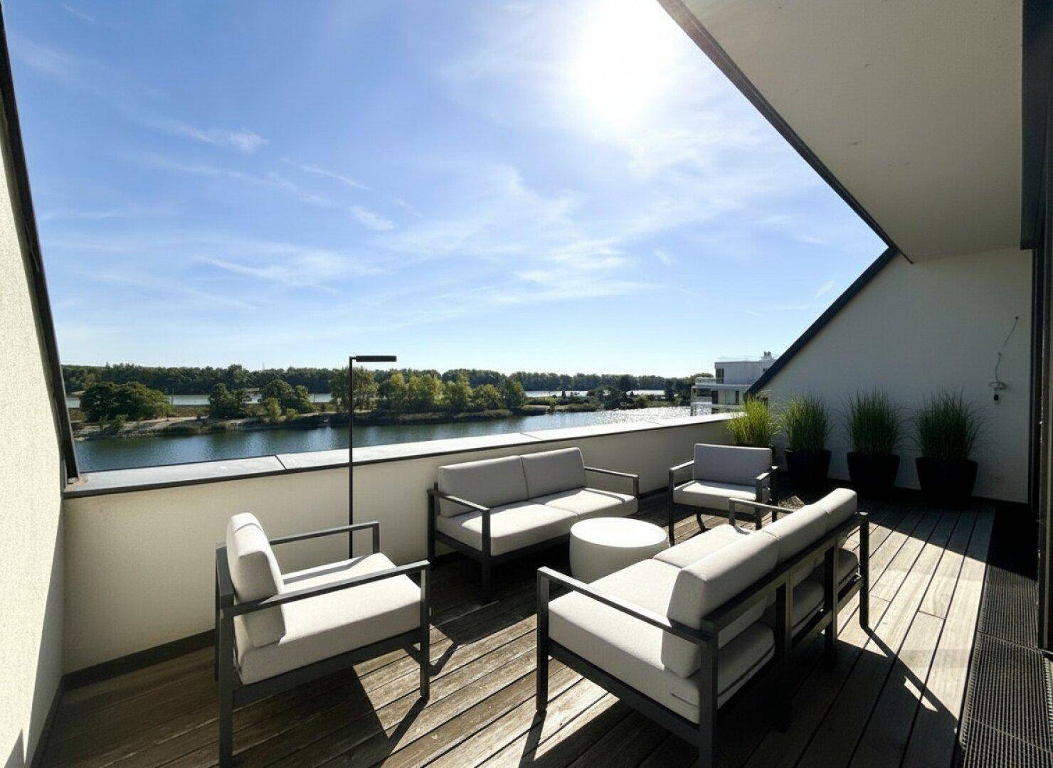 Geräumige Terrasse mit modernen Lounge-Möbeln und Panoramablick auf das Wasser und die Landschaft.